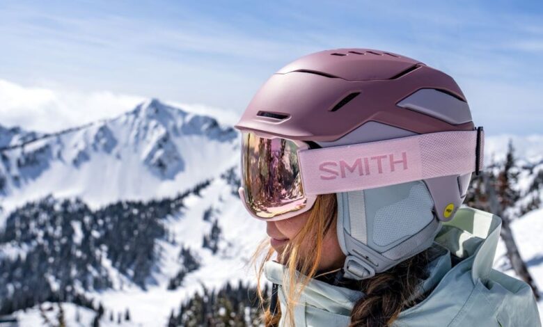 A skier wearing a white Smith Vantage helmet smiles on a sunny mountain, with wireless audio chips seamlessly integrated into the earpads