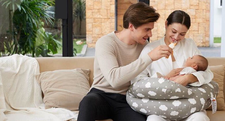 Happy mom smiling while breastfeeding newborn on Momcozy ergonomic nursing pillow in sunny nursery