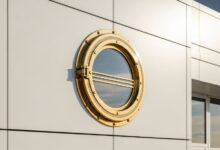 Circular porthole window with brass frame installed in white modern building facade showing art deco streamline design influence