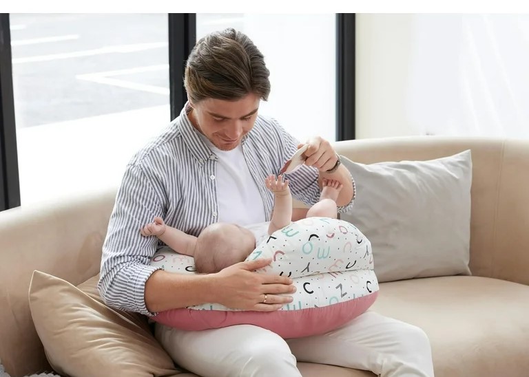 Twin mom comfortably tandem nursing two babies using wide Momcozy breastfeeding support pillow