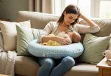 New mom comfortably breastfeeding her baby using a supportive nursing pillow on a couch, demonstrating relaxed posture and proper alignment