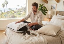 Man sitting in a bright bedroom inspecting two organic buckwheat pillows.